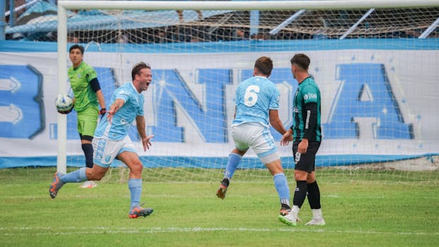 Soccer players celebrating a goal during an outdoor match, expressing joy and teamwork.