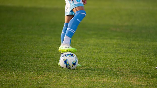 Soccer player in action pose with ball on green field, wearing blue kit.