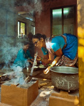 Women in vibrant attire cook traditional meals in a rustic kitchen in Ratnagiri, India.