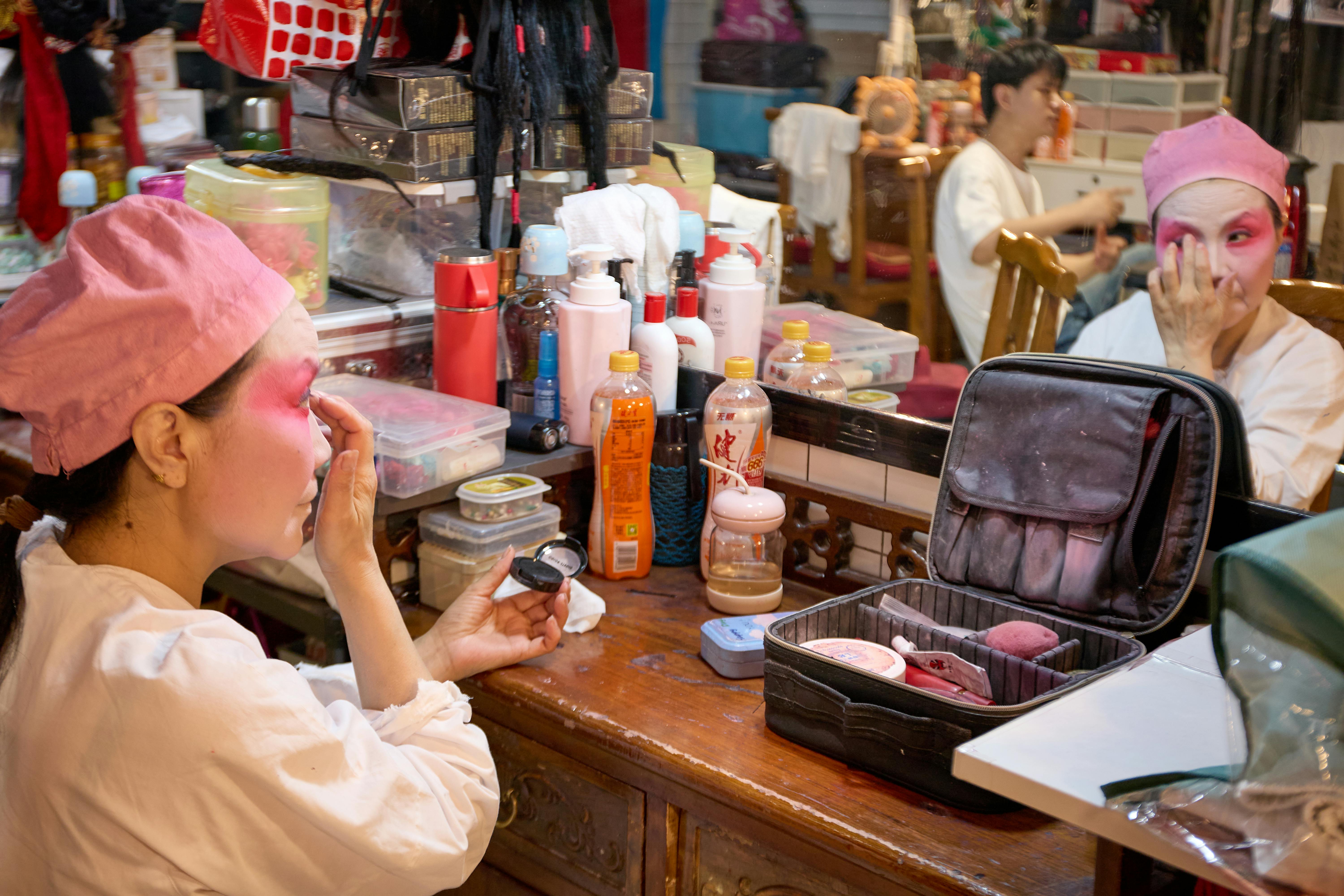 Kostenlos Eine Darstellerin trägt in einer geschäftigen Garderobe leuchtendes Bühnen-Make-up auf. Stock-Foto