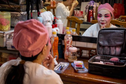 A Chinese opera performer applies makeup backstage in preparation for a performance. Vibrant colors and traditional attire.
