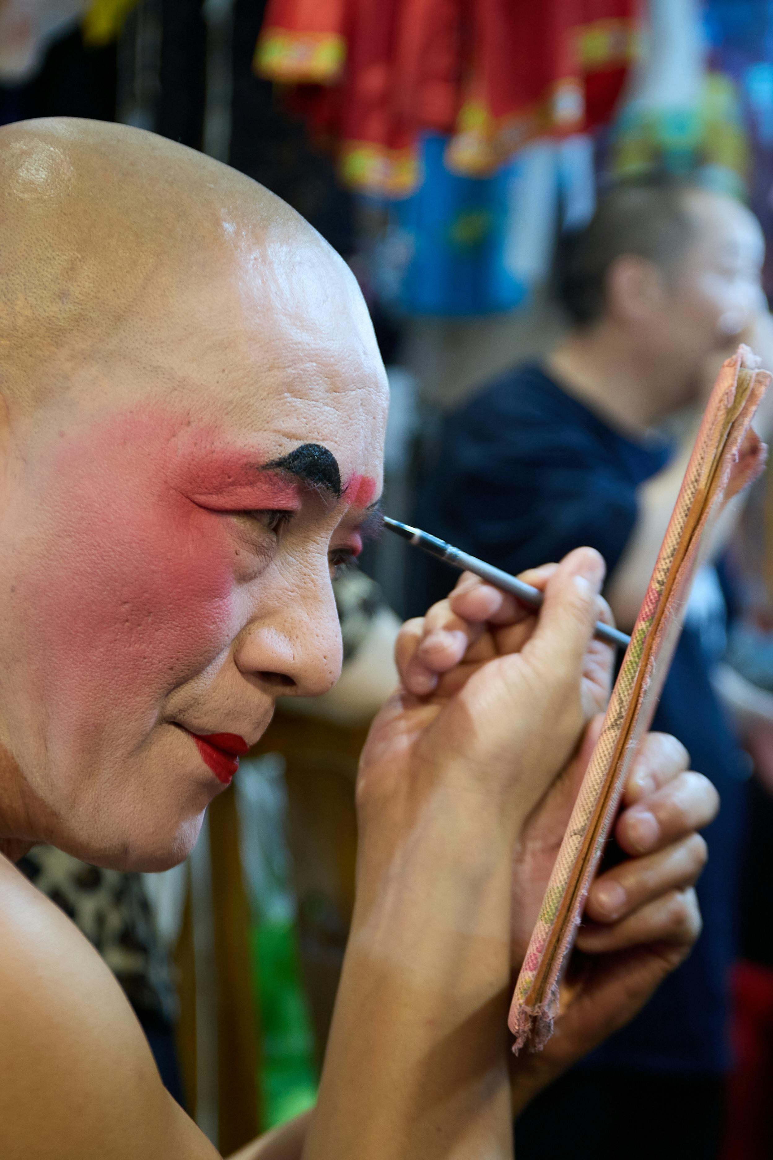 Free A performer applies traditional theatrical makeup in an artistic setting, highlighting cultural artistry. Stock Photo