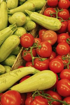 Vibrant arrangement of fresh green zucchinis and ripe red tomatoes at an outdoor market.