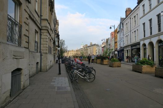 A picturesque urban street lined with bicycles, shops, and pedestrians enjoying a pleasant day.