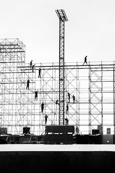 Silhouetted workers on scaffolding against the sky, depicting urban construction dynamics.