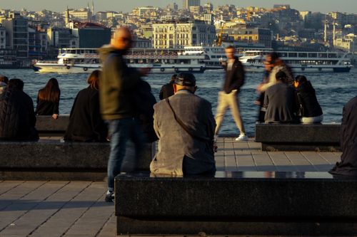 Free People sitting and walking by a bustling waterfront with ferries and cityscape in the background. Stock Photo