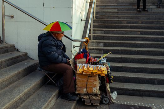 A street vendor seated on steps under a colorful umbrella, displaying various items for sale.