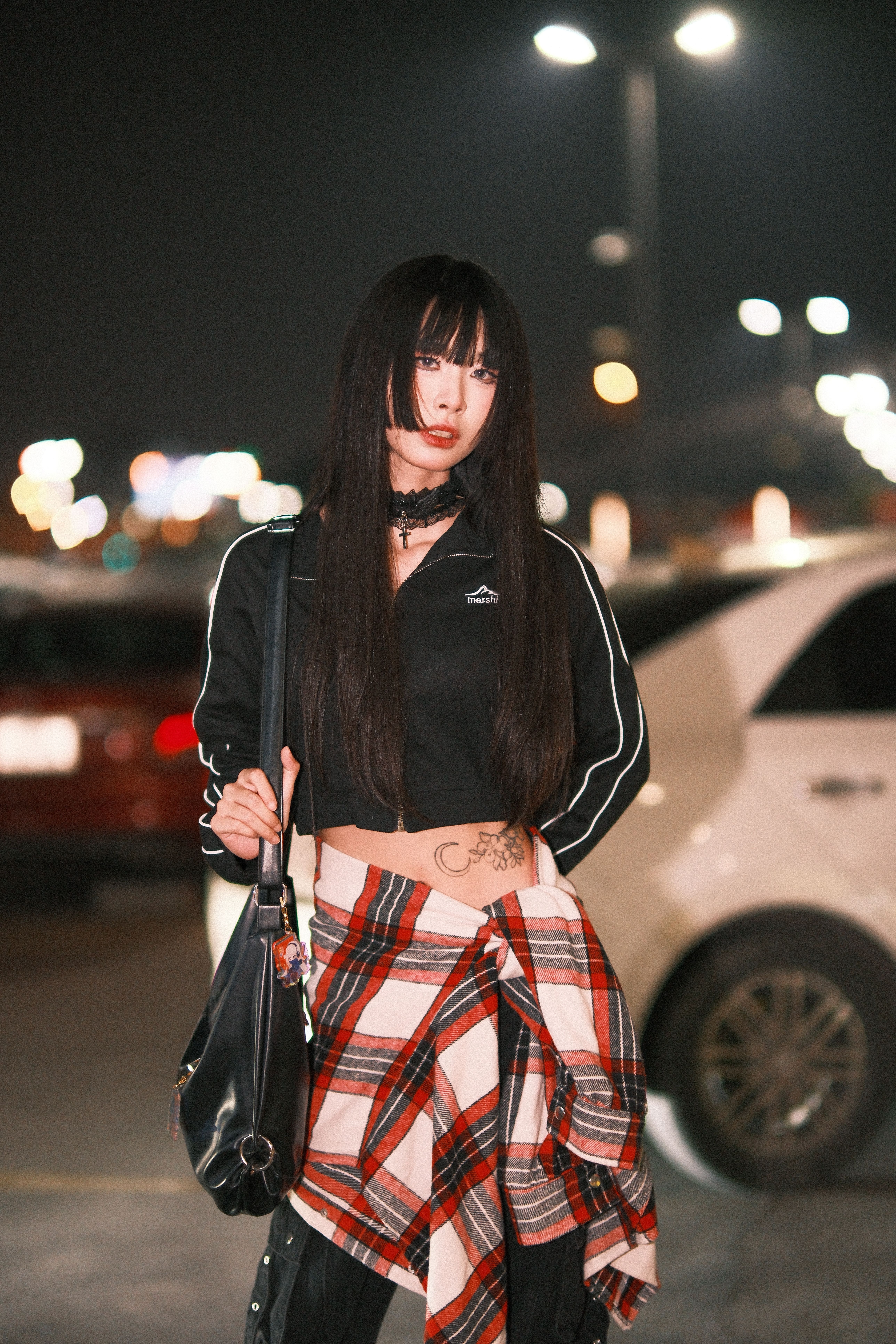 Stylish young woman poses confidently in a nighttime urban parking lot.
