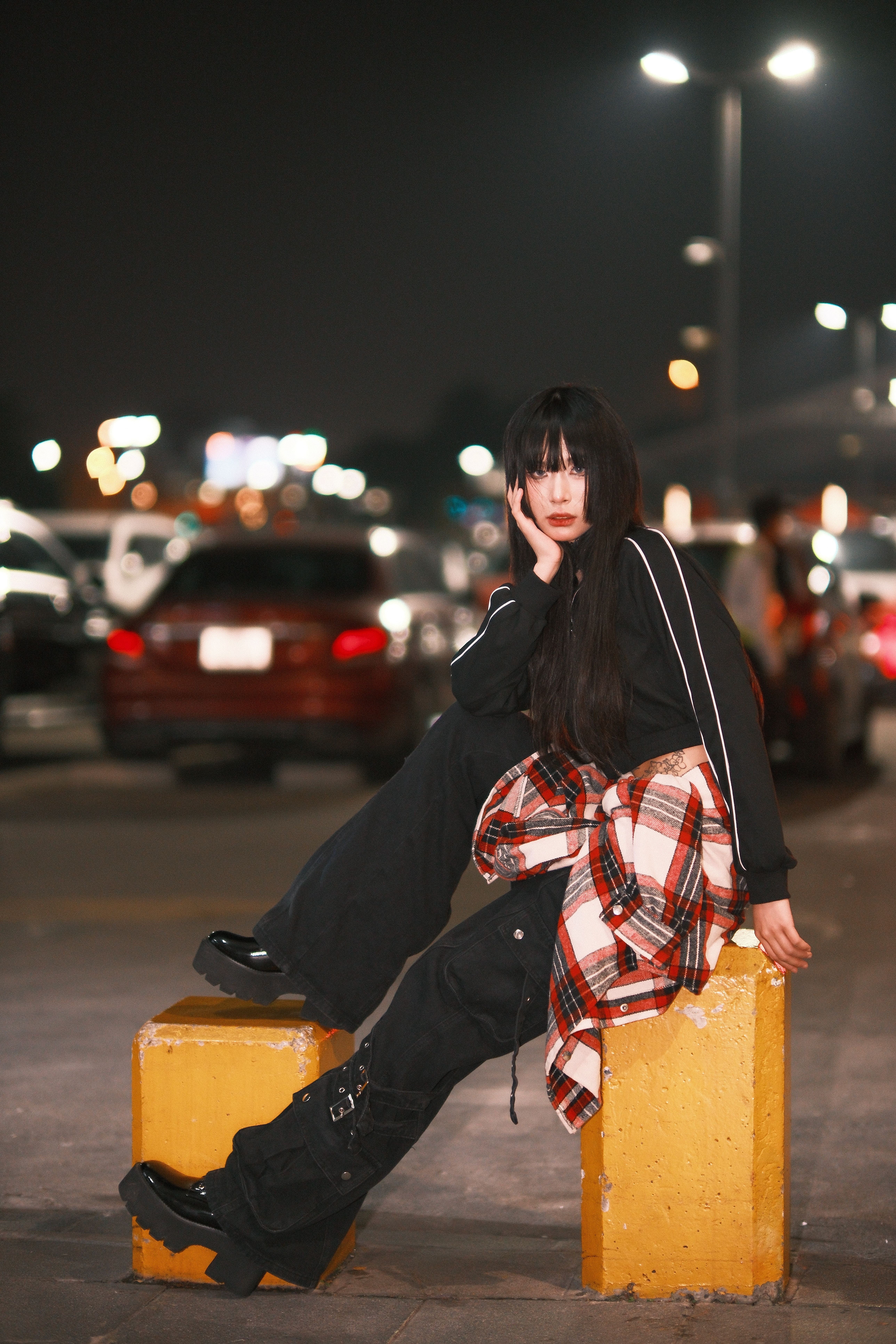 A young woman in trendy attire poses in a lit street at night, exuding confidence and style.