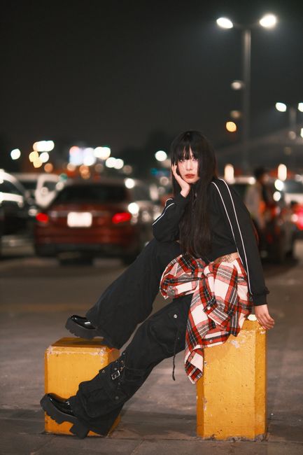 A young woman in trendy attire poses in a lit street at night, exuding confidence and style.