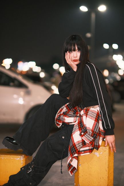 Fashionable young woman posing on city street at night, embracing urban style.