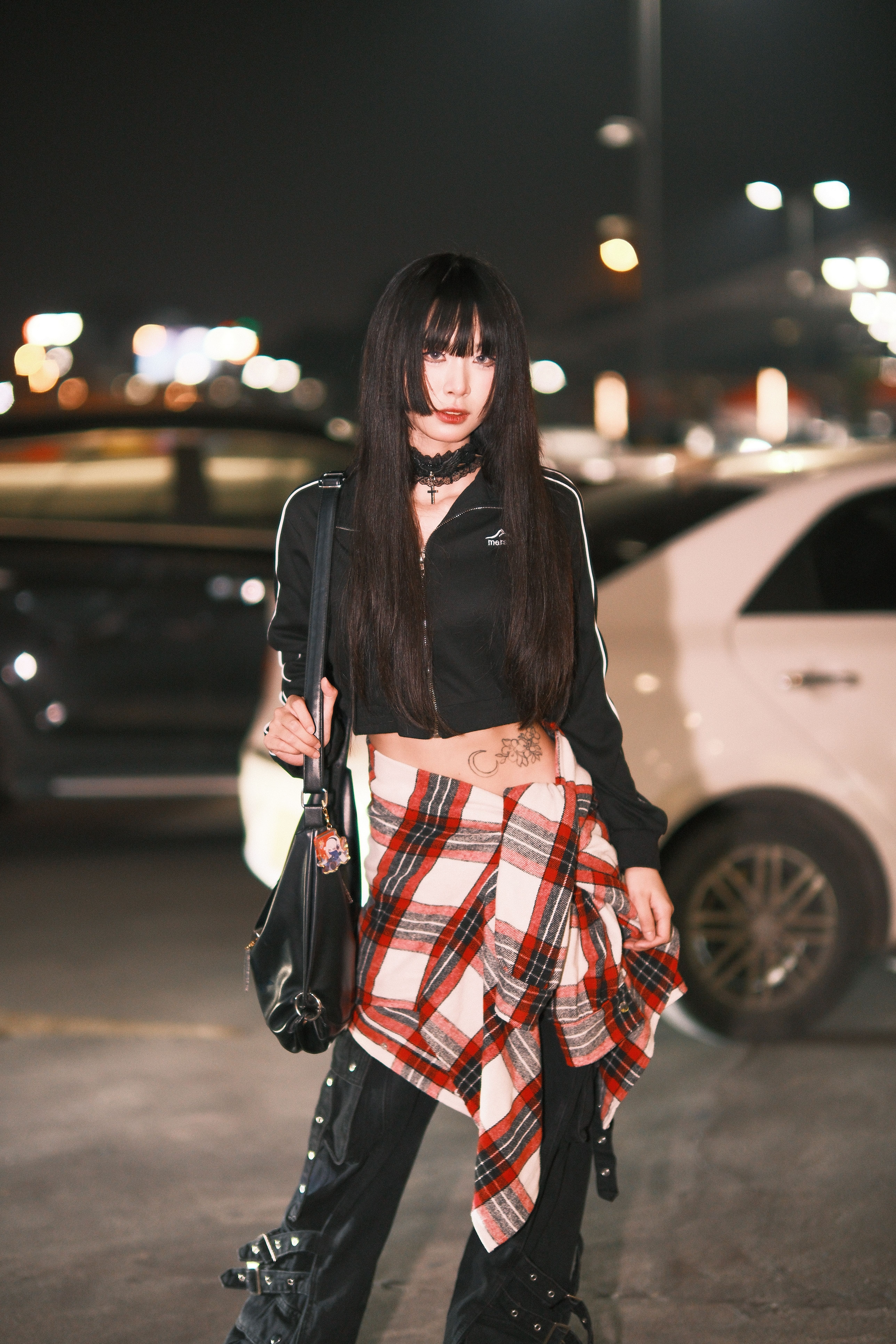 A fashionable woman stands confidently in a nighttime urban parking lot, showcasing modern streetwea