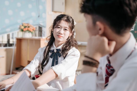 Two high school students in uniform engaged in a classroom discussion.