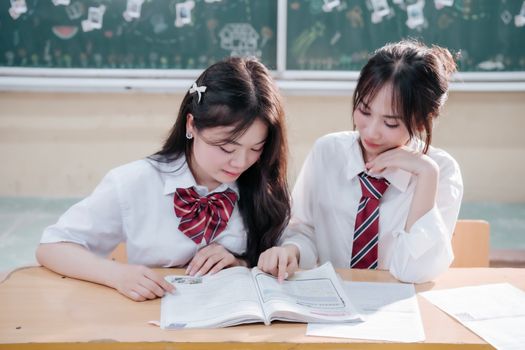 Two female students in uniform studying together in a classroom setting, promoting education.