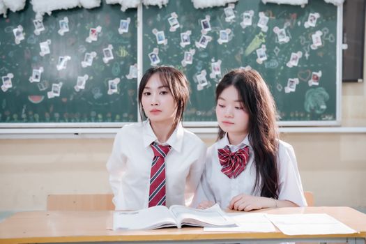 Two students in uniforms sitting at a desk with books in a classroom setting.