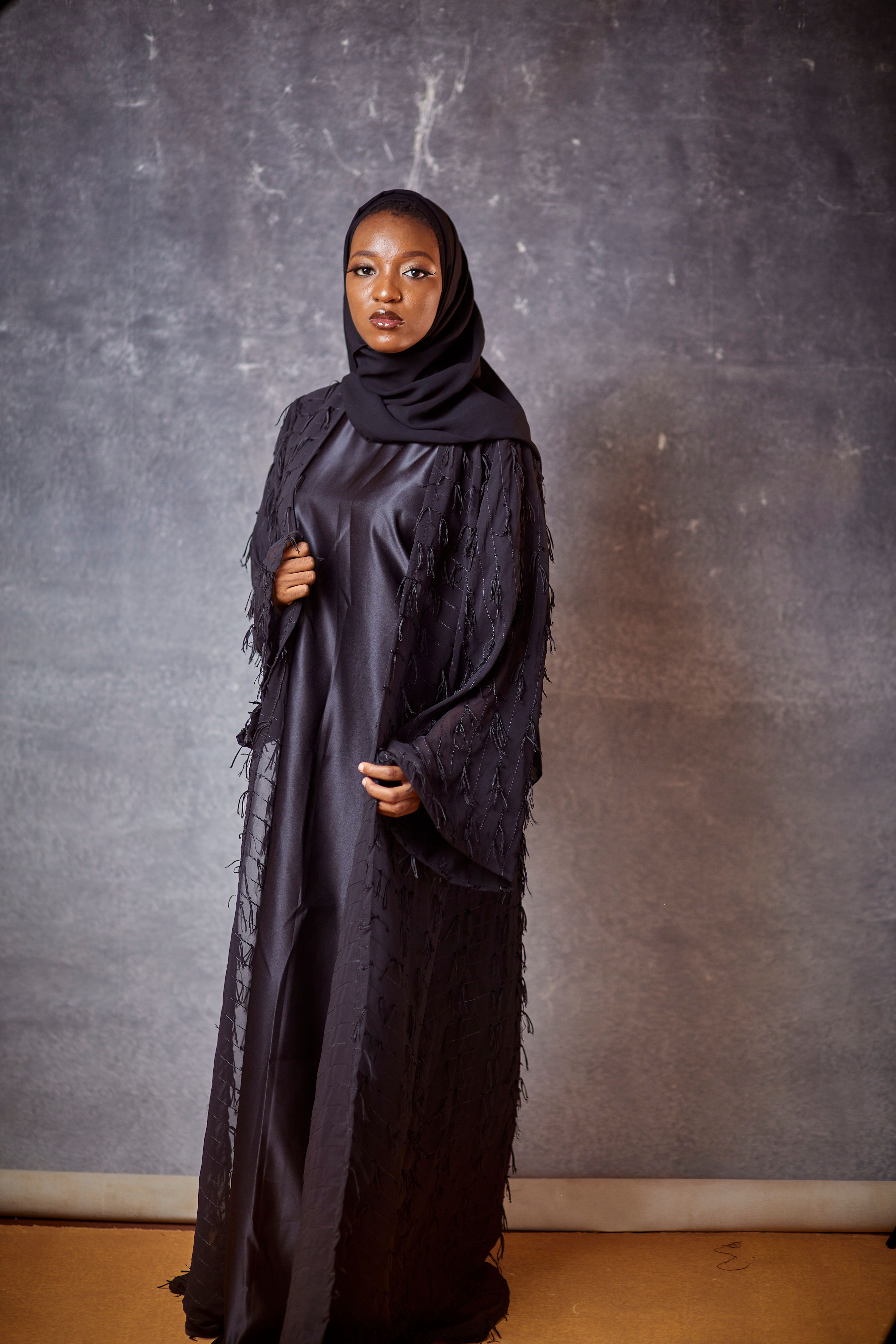 Woman wearing a tailored black abaya against a neutral studio backdrop