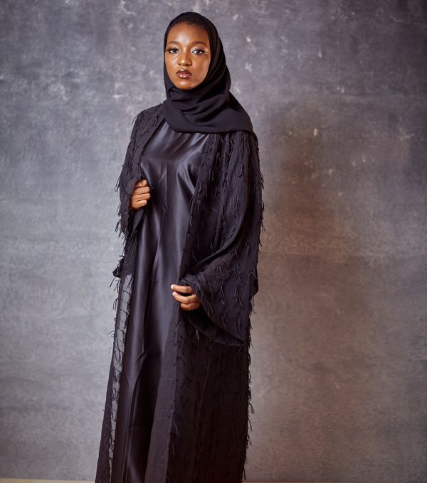 Woman wearing a tailored black abaya against a neutral studio backdrop