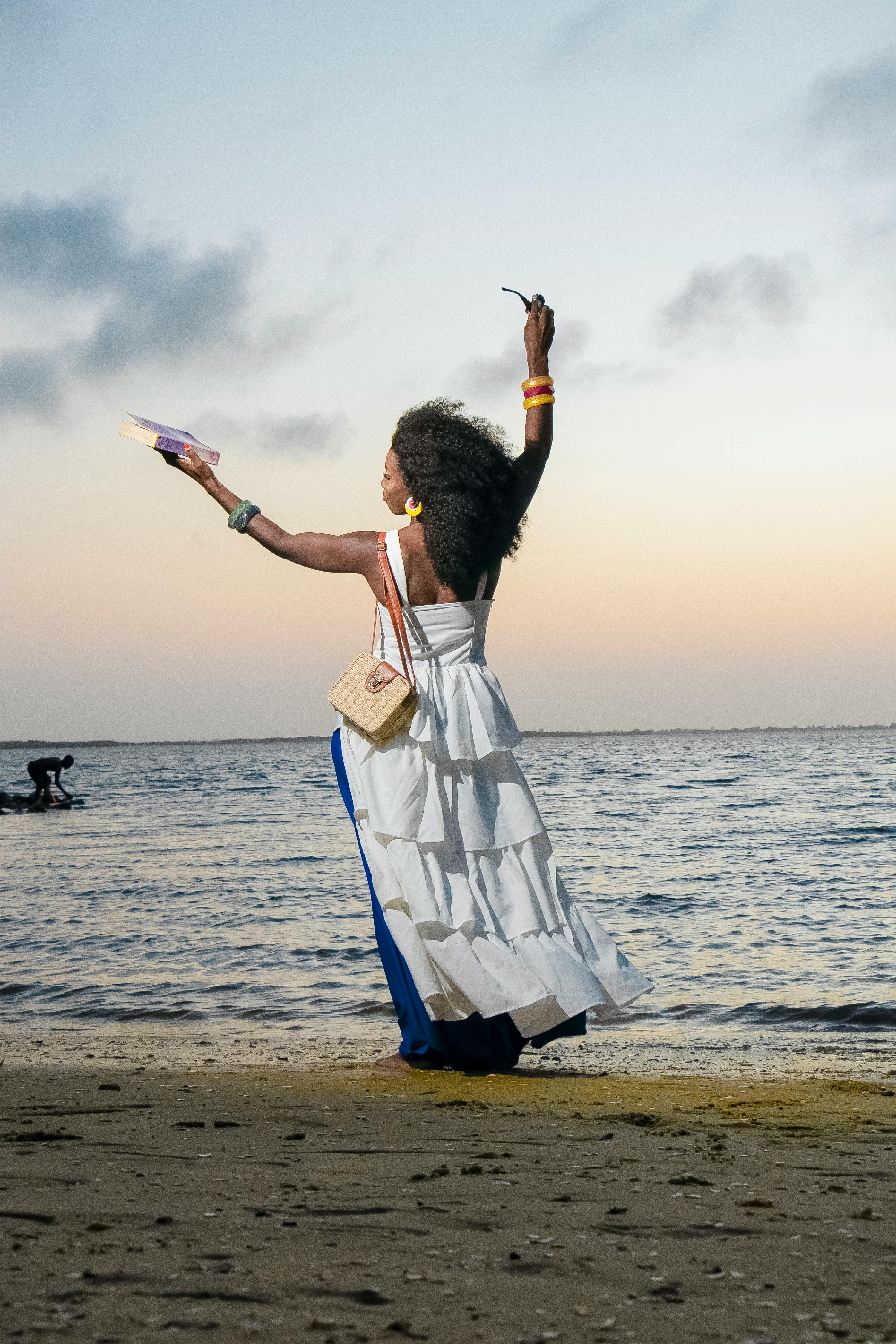 Joyful woman in white dress celebrates at sunset on a serene Burkina Faso beach.