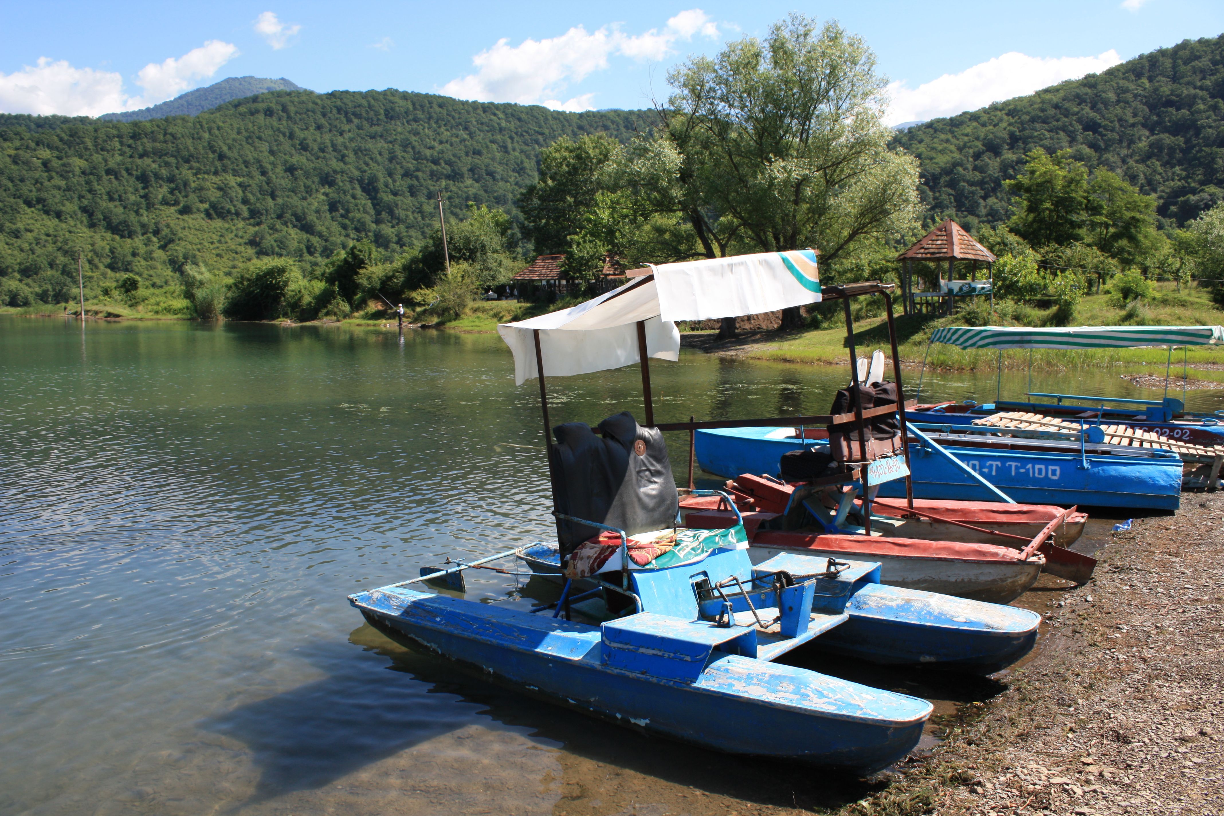 Vibrant pedal boats on a serene lake with lush green mountains in summer.