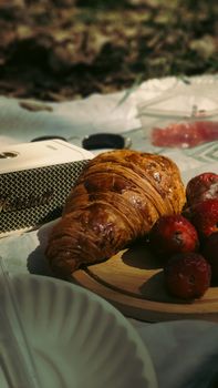 Fresh croissant with strawberries at a picnic with vintage speaker.