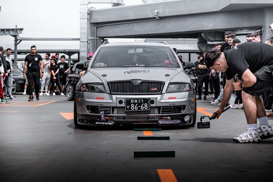 Car enthusiasts gather around a modified car at an outdoor meetup.