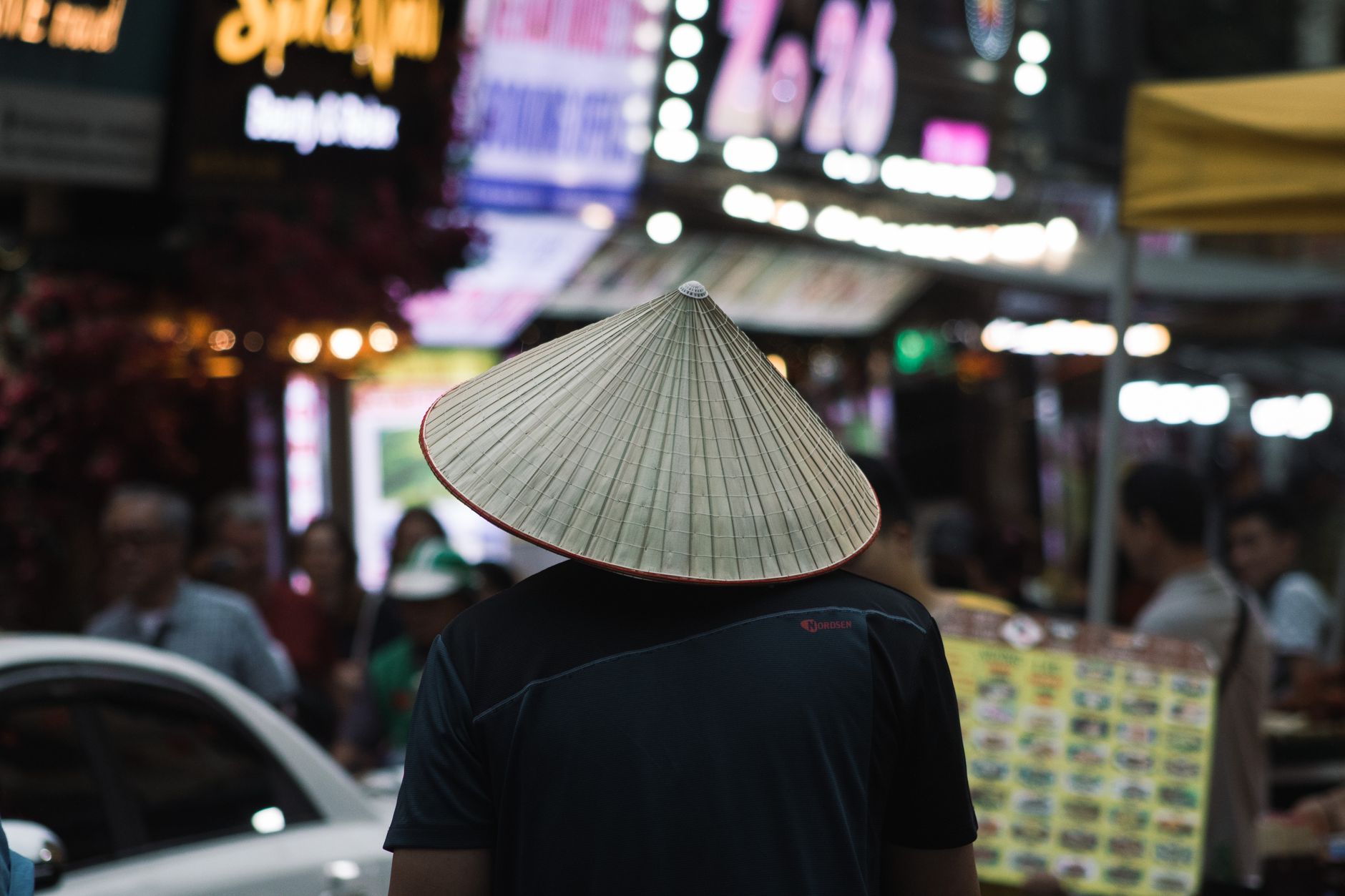 Man wearing traditional Vietnamese hat at Hanoi night market. Vibrant street life captured.