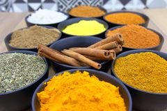 Colorful assortment of spices in bowls with cinnamon sticks on a wooden surface.
