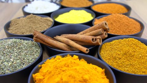 Colorful assortment of spices in bowls with cinnamon sticks on a wooden surface.