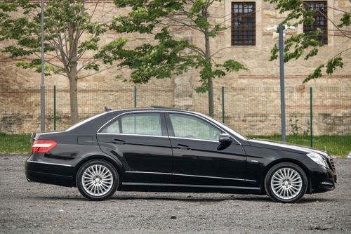 Free Side view of a luxury black sedan parked outdoors against a historic building background. Stock Photo