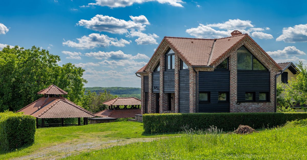 Beautiful brick house with red roof in scenic green landscape under a bright blue sky.
