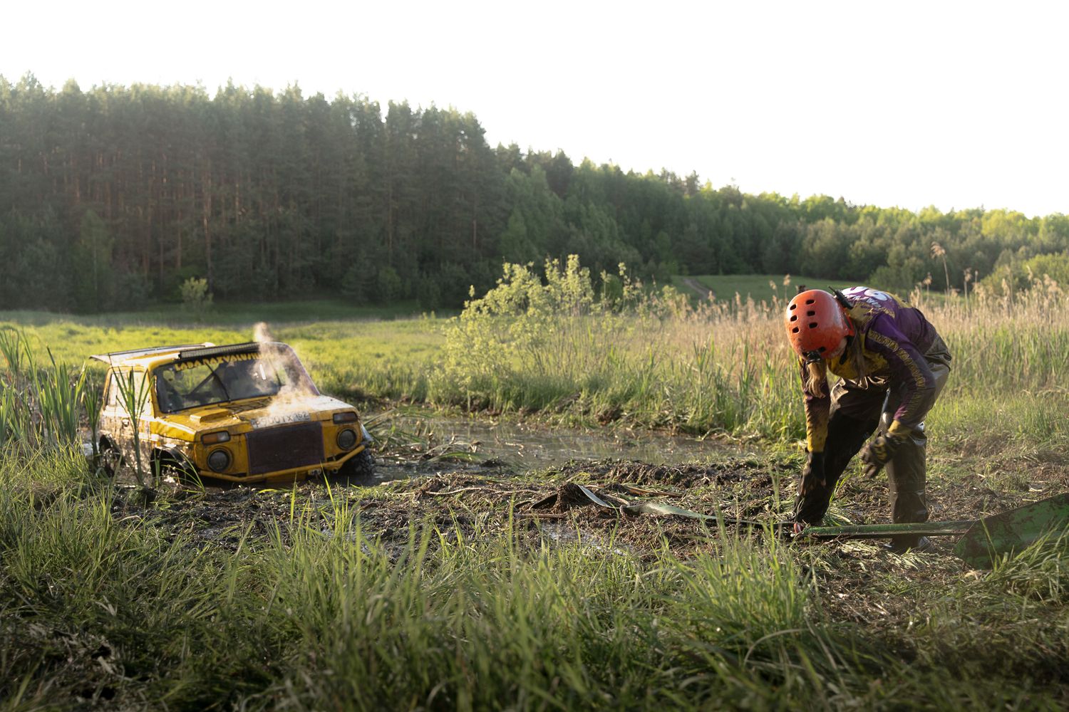4x4 off-road vehicle deeply stuck in thick mud with a driver preparing for recovery