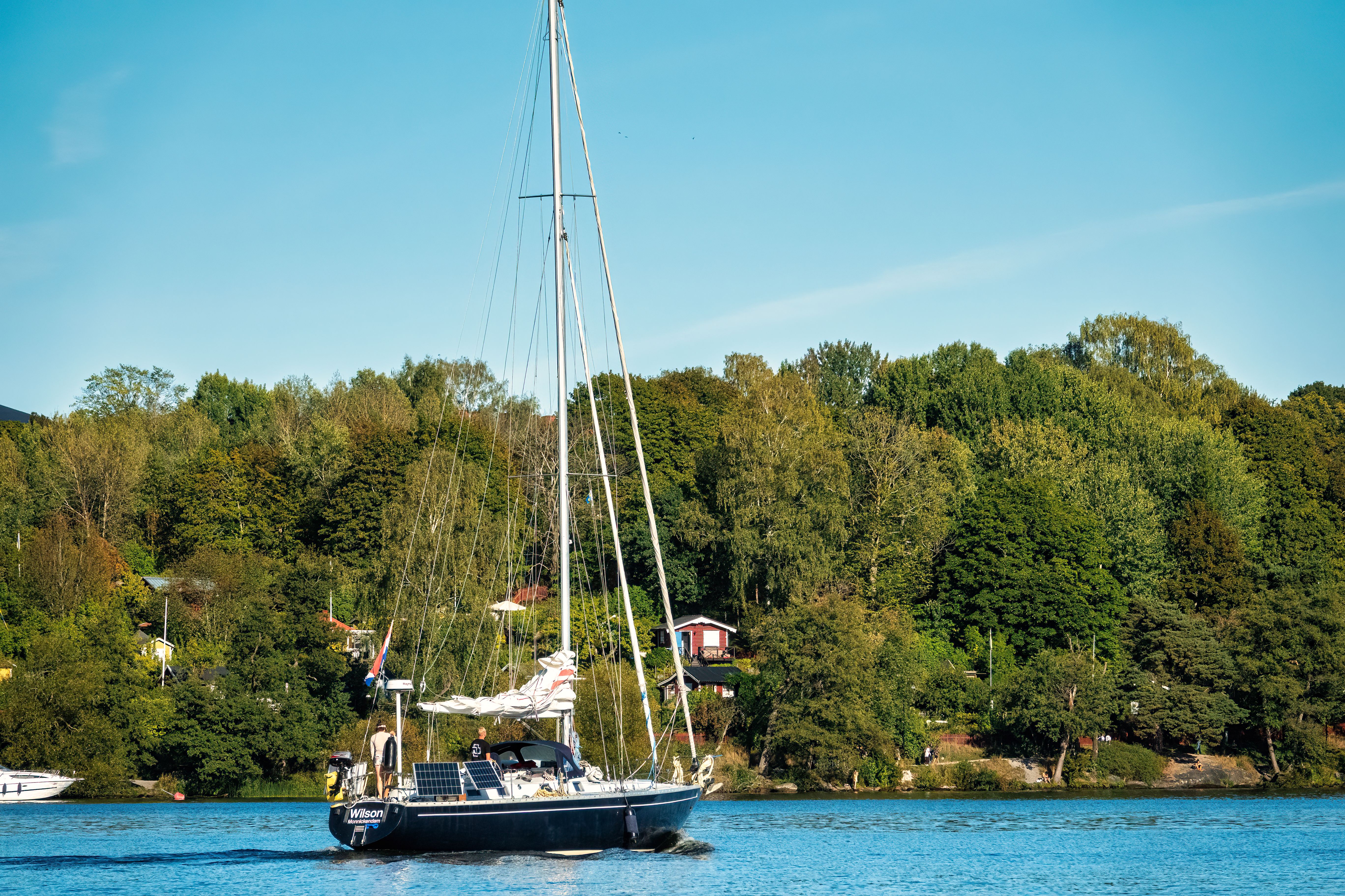 A yacht sails through the calm waters of Stockholm Archipelago surrounded by lush greenery.
