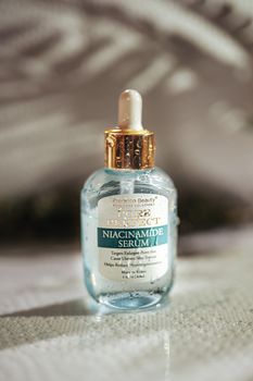 Close-up of a Precision Beauty Niacinamide Serum bottle with a golden cap on a textured surface.