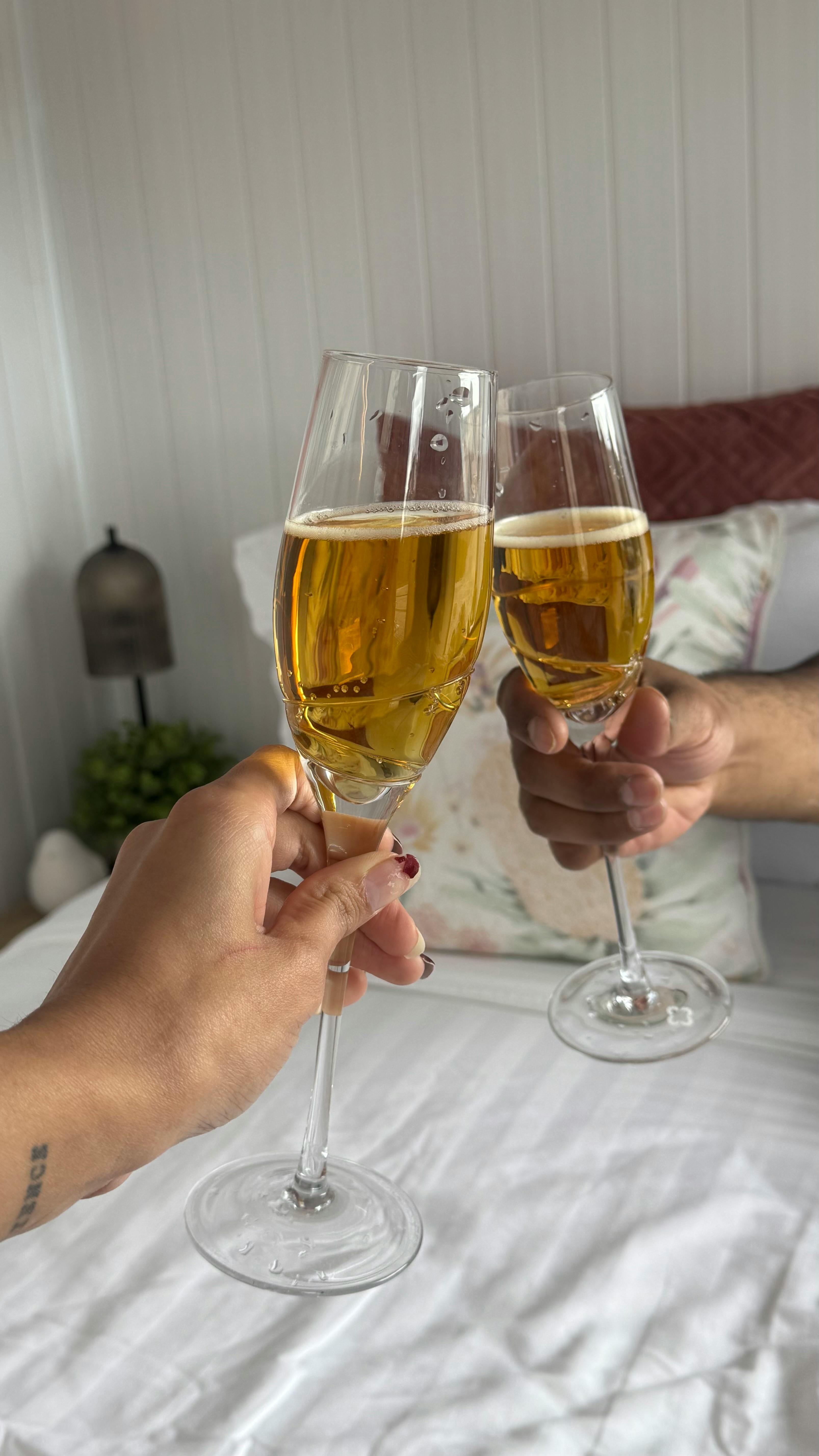 Close-up of two people toasting with champagne flutes in an intimate bedroom ambiance.