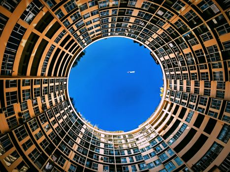 Stunning upward view of circular building with a plane in the blue sky.