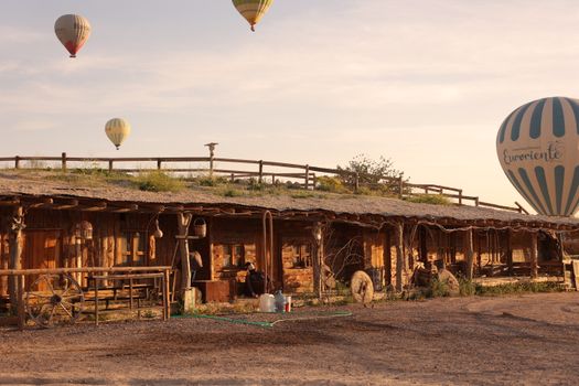 Rustic cabin in Cappadocia with hot air balloons floating in the warm sunrise.