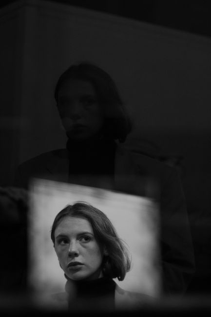 A thoughtful woman gazes with a reflection in a moody black and white setting.