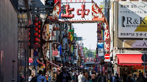Free Bustling street in Tokyo filled with signs, shops, and people under red maple archway. Stock Photo