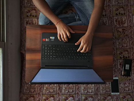 Aerial view of individual typing on a laptop, legs crossed on a patterned floor.