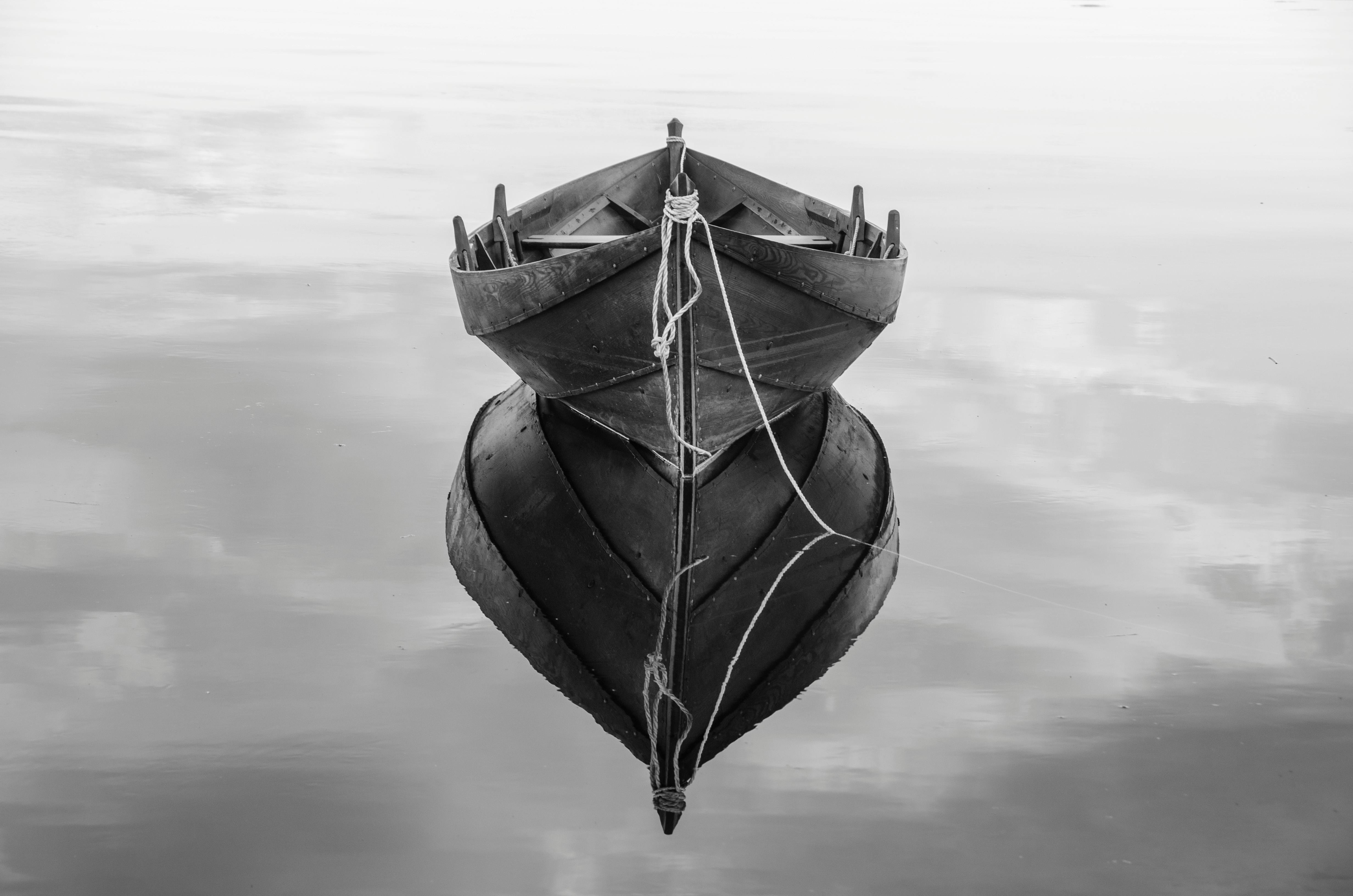 Elegant black and white photo of a boat with a perfect symmetrical reflection on calm water.