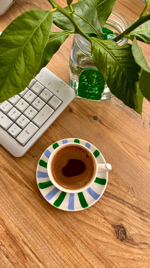 Free A warm, inviting workspace featuring a cup of coffee, a keyboard, and lush green leaves. Stock Photo