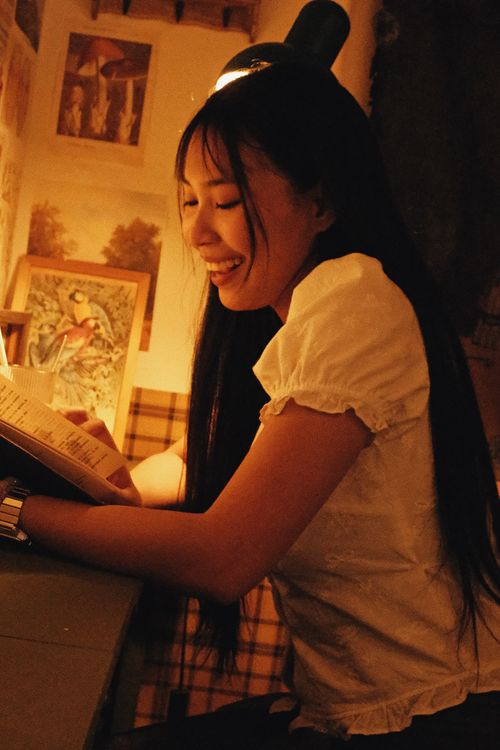 Free A young woman enjoys reading in a cozy, warmly lit room with artistic wall decor. Stock Photo