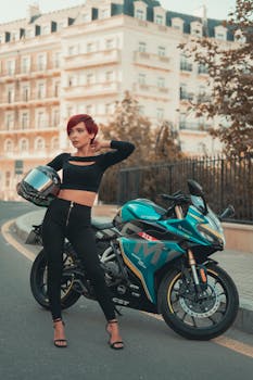 Stylish woman with red hair poses next to a sleek sport motorcycle in an urban setting.