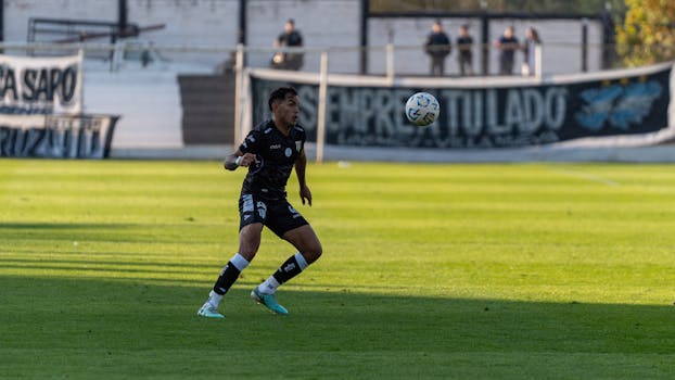 Energetic soccer player in black kit focused on the ball during an outdoor match.
