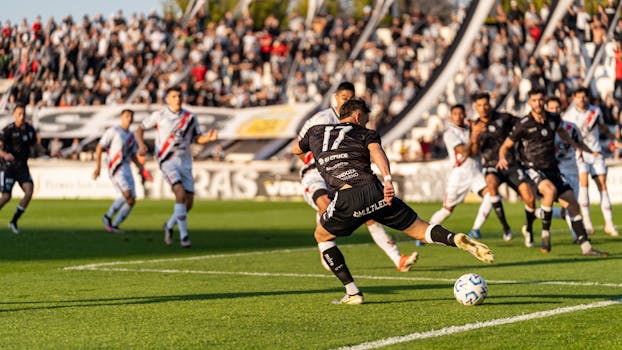 A dynamic football match with players in motion on a sunny day, witnessed by a packed stadium.