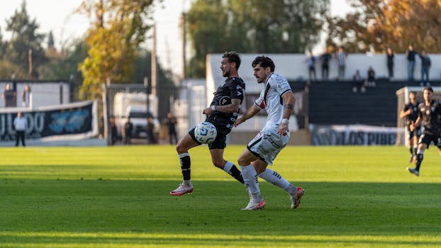 Two soccer players competing for the ball on the field during an outdoor match.