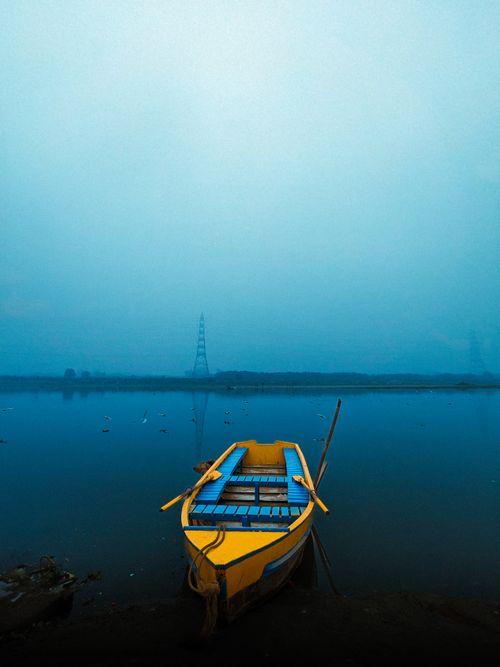 Free A vibrant yellow boat rests peacefully on still blue waters in Delhi, India, under a clear sky. Stock Photo