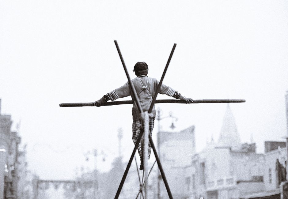 A dramatic scene of a man balancing on a tightrope in Ayodhya, capturing the urban backdrop and traditional street performance.