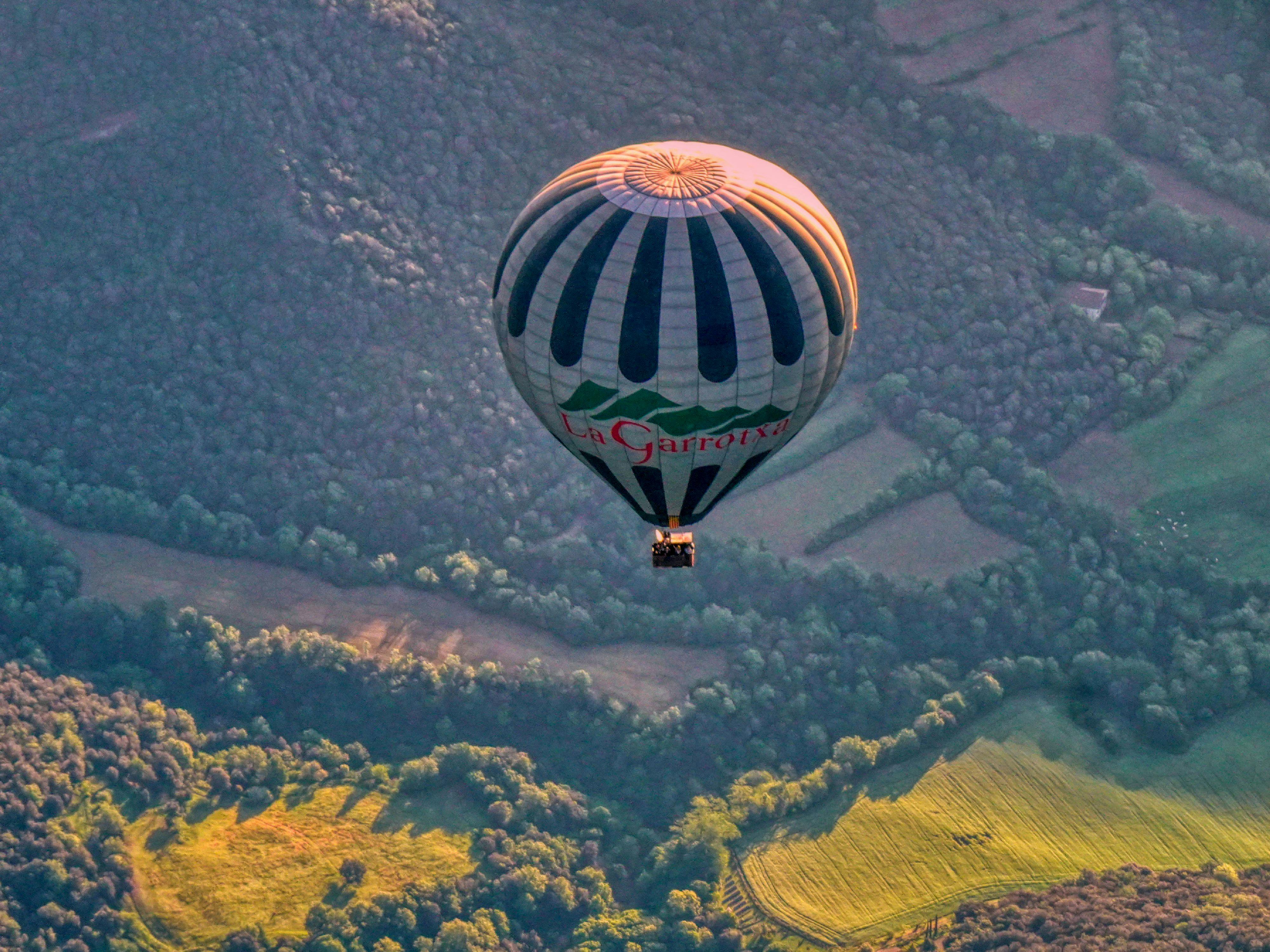 Hot air balloon soaring over lush landscapes of Santa Pau, Catalonia at sunrise.
