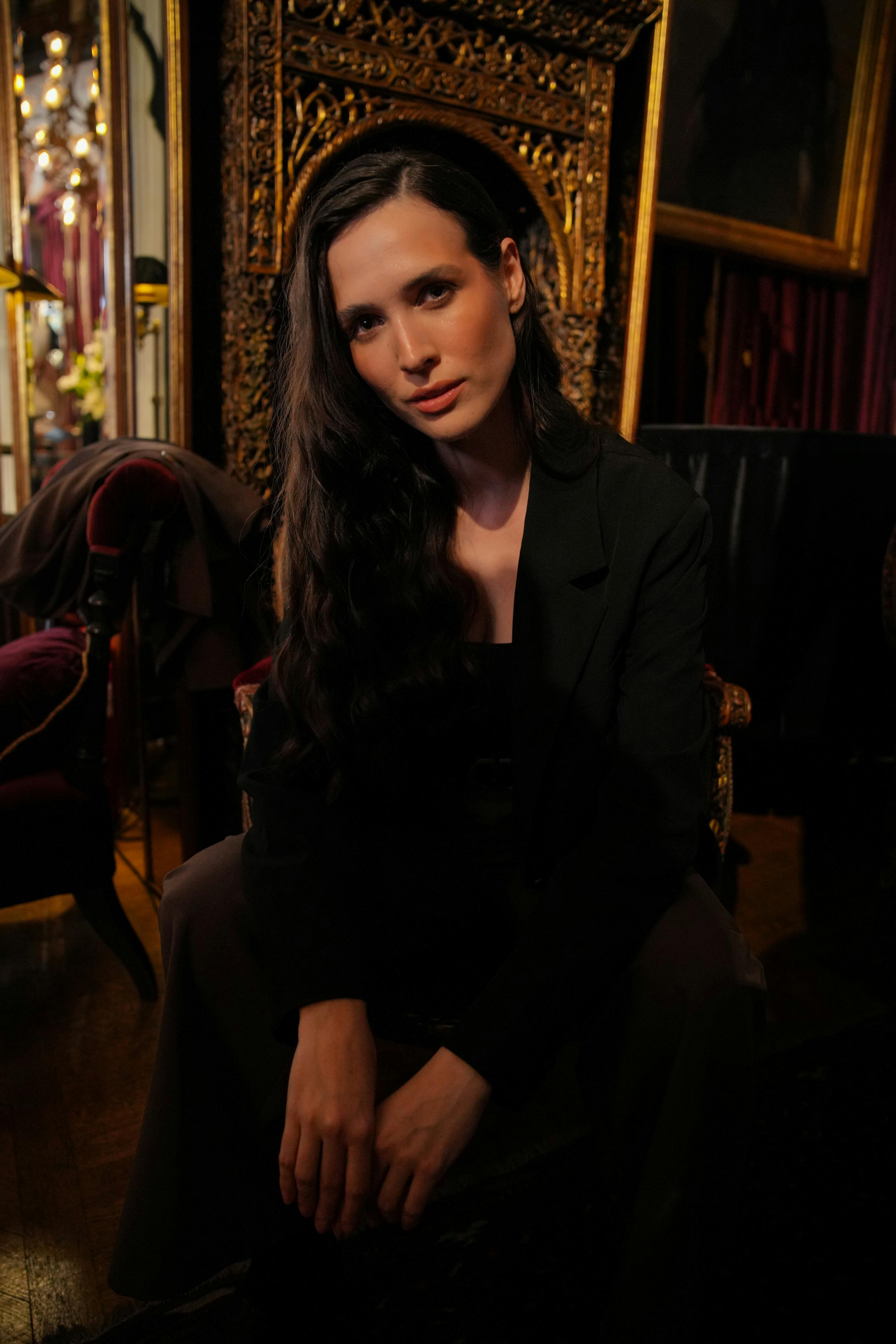 Gratuit Femme sophistiquée assise dans une pièce ornée, faiblement éclairée et au décor riche. Photos